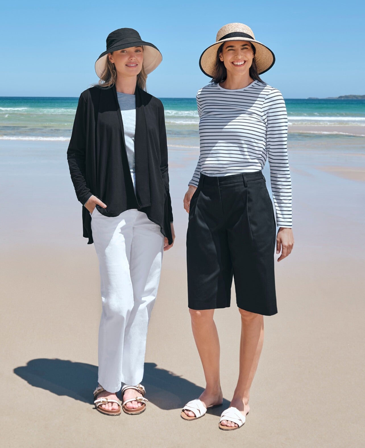 Two women standing on a beach wearing Solbari sun hats and sun protective casual clothing.